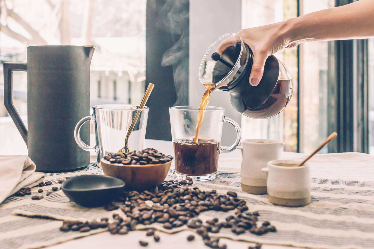 Why Fresh Coffee Roasting Makes Mornings Magical - Pouring freshly brewed coffee into a cup surrounded by coffee beans.
