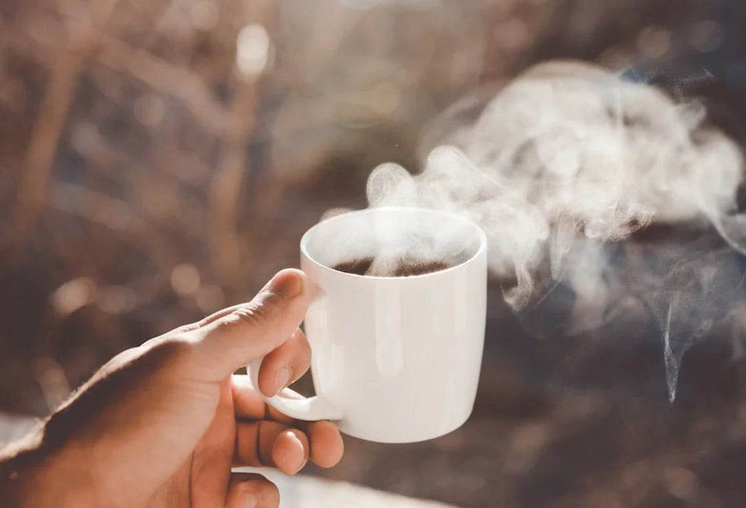 Decaf Coffee - What you need to know - steaming cup of decaf coffee held in hand outdoors.