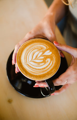 Spilled dark coffee beans on a rustic wooden table with lush green coffee plants