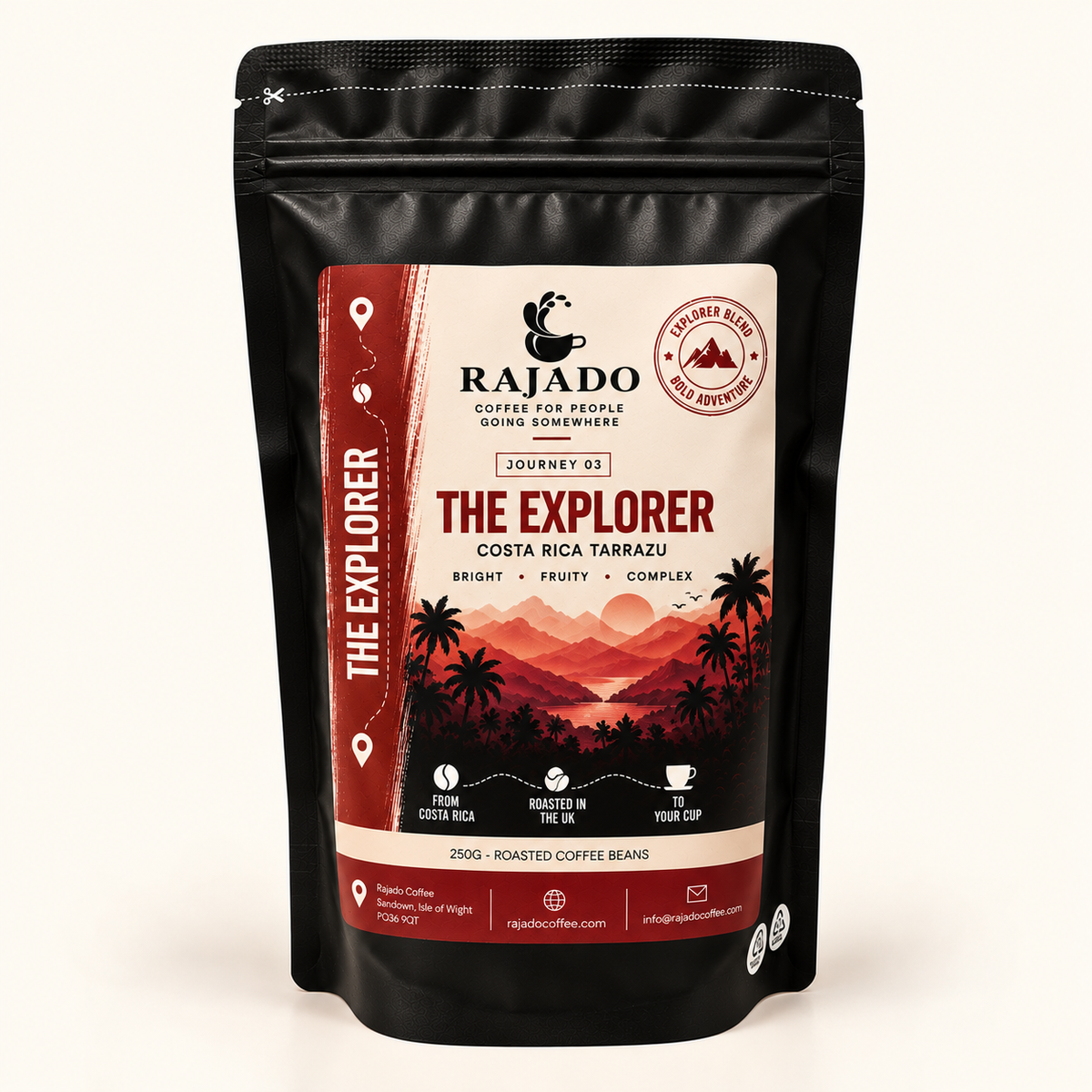 A black stand-up pouch of Rajado Coffee Roasters 'The Explorer' Costa Rica Tarkaku coffee beans, featuring a cream and red label with a sunset mountain illustration, set against a plain off-white background.